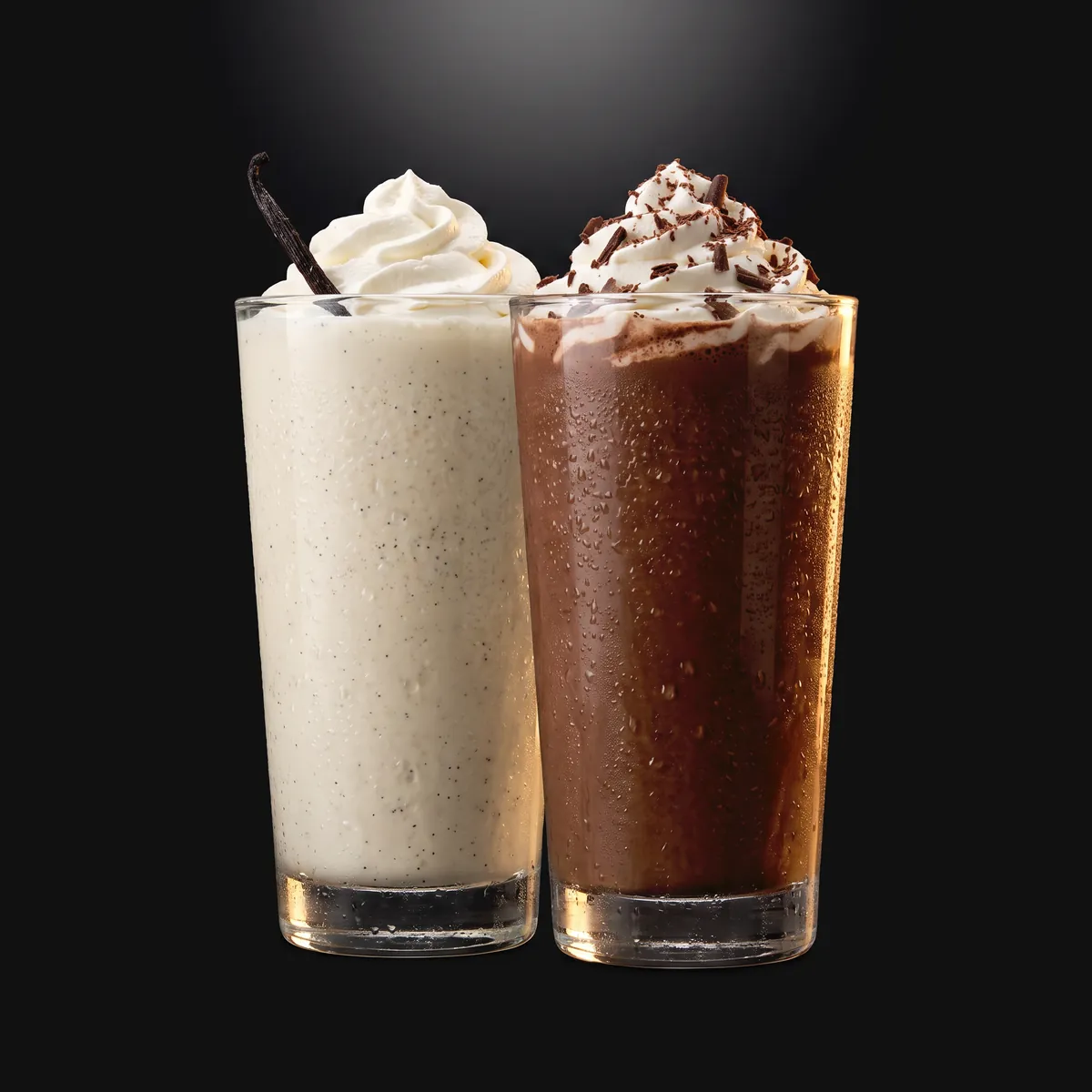 A vanilla shake and a chocolate shake, both topped with whipped cream.