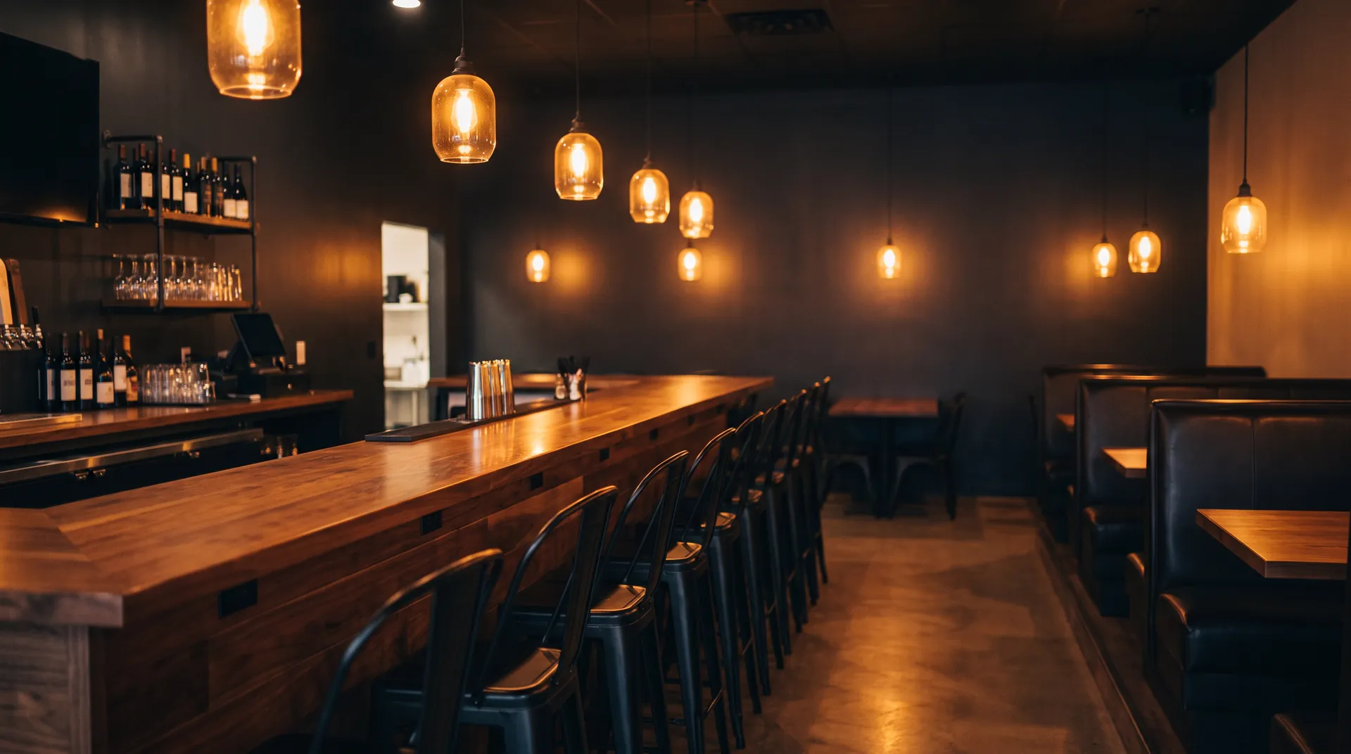 The dining room at night: a long wooden counter, bar stools and low amber pendant lights.